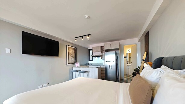 A modern hotel room with a large bed, a TV mounted on the wall, a kitchenette, and a bathroom with a mirror and sink. - w* | Bright Loft in Santa Ana w/ AC (Panamá)