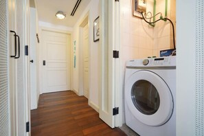 A laundry room with a front-loading washing machine, a door with a handle, and a wall-mounted light fixture.