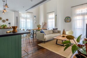 A spacious living area with a sofa, coffee table, and dining table. There are potted plants and artwork on the walls.