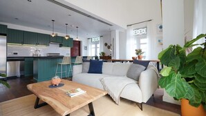 Une cuisine moderne avec des meubles de couleur verte, un coin repas avec une table en bois et un salon avec un canapé et une grande plante.