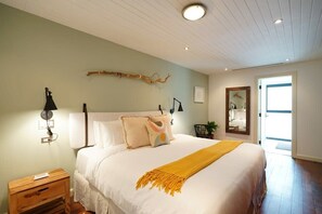 A bedroom with a bed, bedside lamps, a nightstand, a mirror, and a door leading to another room.