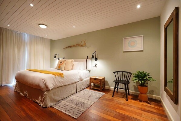 A bedroom with a large bed, bedside tables, a chair, a potted plant, and a framed picture on the wall.