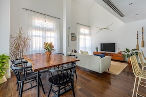 Una sala de estar moderna con una mesa de comedor de madera, sillas negras, un sofá y un televisor.