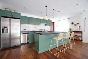 Una cocina moderna con armarios verdes, electrodomésticos de acero inoxidable y una isla central con taburetes de bar.