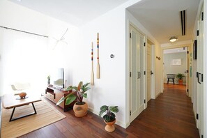 Una sala de estar moderna con piso de madera, una mesa de comedor y un sofá. Se observan varias plantas en macetas y un televisor sobre un mueble.