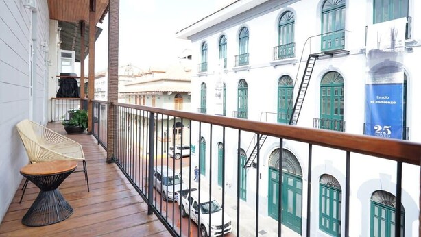 Un balcon avec une balustrade en bois, une chaise en osier et une plante en pot.