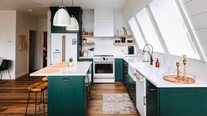 A modern kitchen with a central island, white countertops, and green cabinetry.