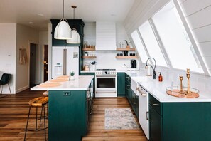 Cocina moderna con una isla central, encimeras blancas y armarios verdes.