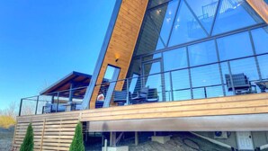 A modern building with large glass windows, wooden deck, and a clear sky.