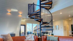 A modern living room with a spiral staircase, leather sofas, and a round wooden coffee table.