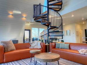 Una sala moderna con una escalera en espiral, sofás de cuero y una mesa de centro redonda de madera.