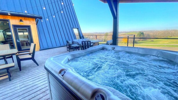 A hot tub on a wooden deck with outdoor seating and a view of the landscape.