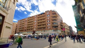 A multi-story building with balconies, a sign for 'Bershka', and a pedestrian area with people and a bicycle. - Suitequarantotto CURS CIN IT063049C2Z4YC4Q9U  (Napoli)