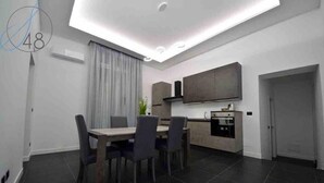 A modern kitchen with dark tiles, a dining area with a table and chairs, and a large window with curtains. - Suitequarantotto CURS CIN IT063049C2Z4YC4Q9U  (Napoli)