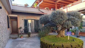 A courtyard with a brick wall, a large tree, and a sign that reads "Bienvenue!" - Midway House Apartment with free internal parking (Sant'Egidio del Monte Albino)