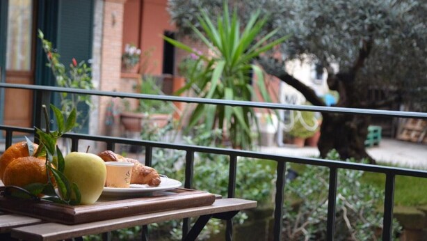 A balcony with a table holding a plate with food and a glass, overlooking a garden with trees and plants. - Midway House Apartment with free internal parking (Sant'Egidio del Monte Albino)