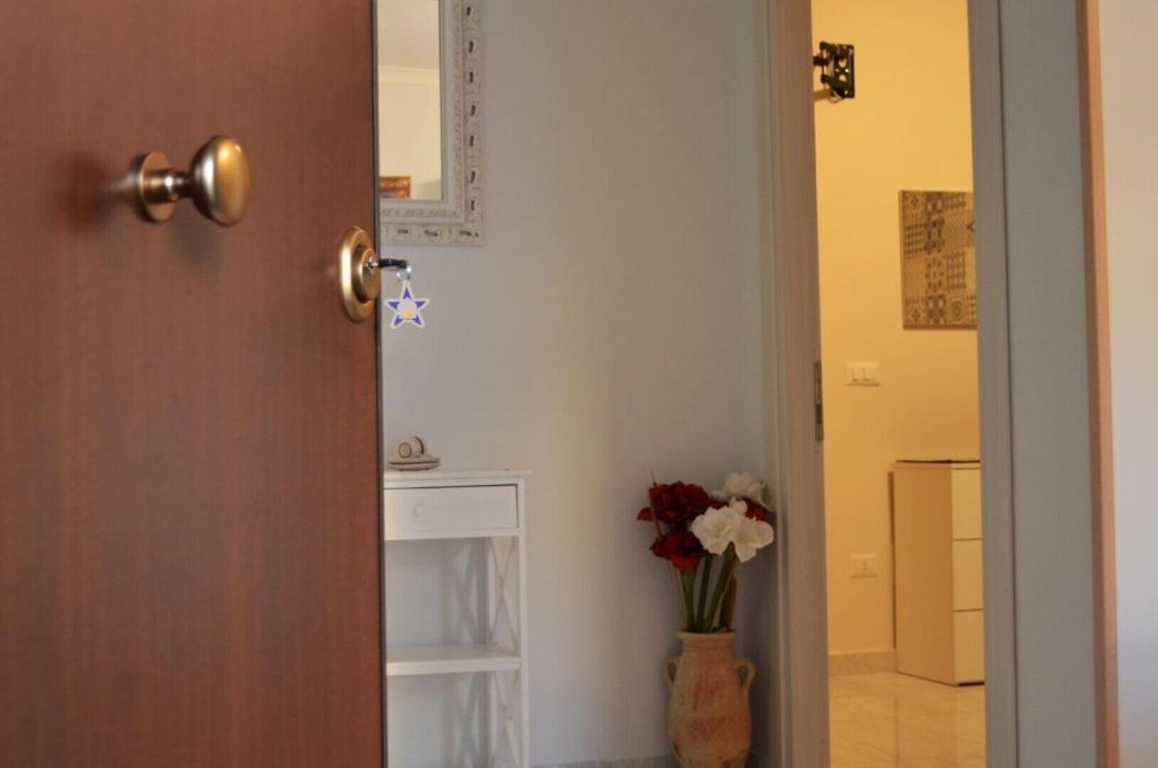A wooden door with a brass handle, a white shelf with a small item on it, and a vase with flowers in the background.