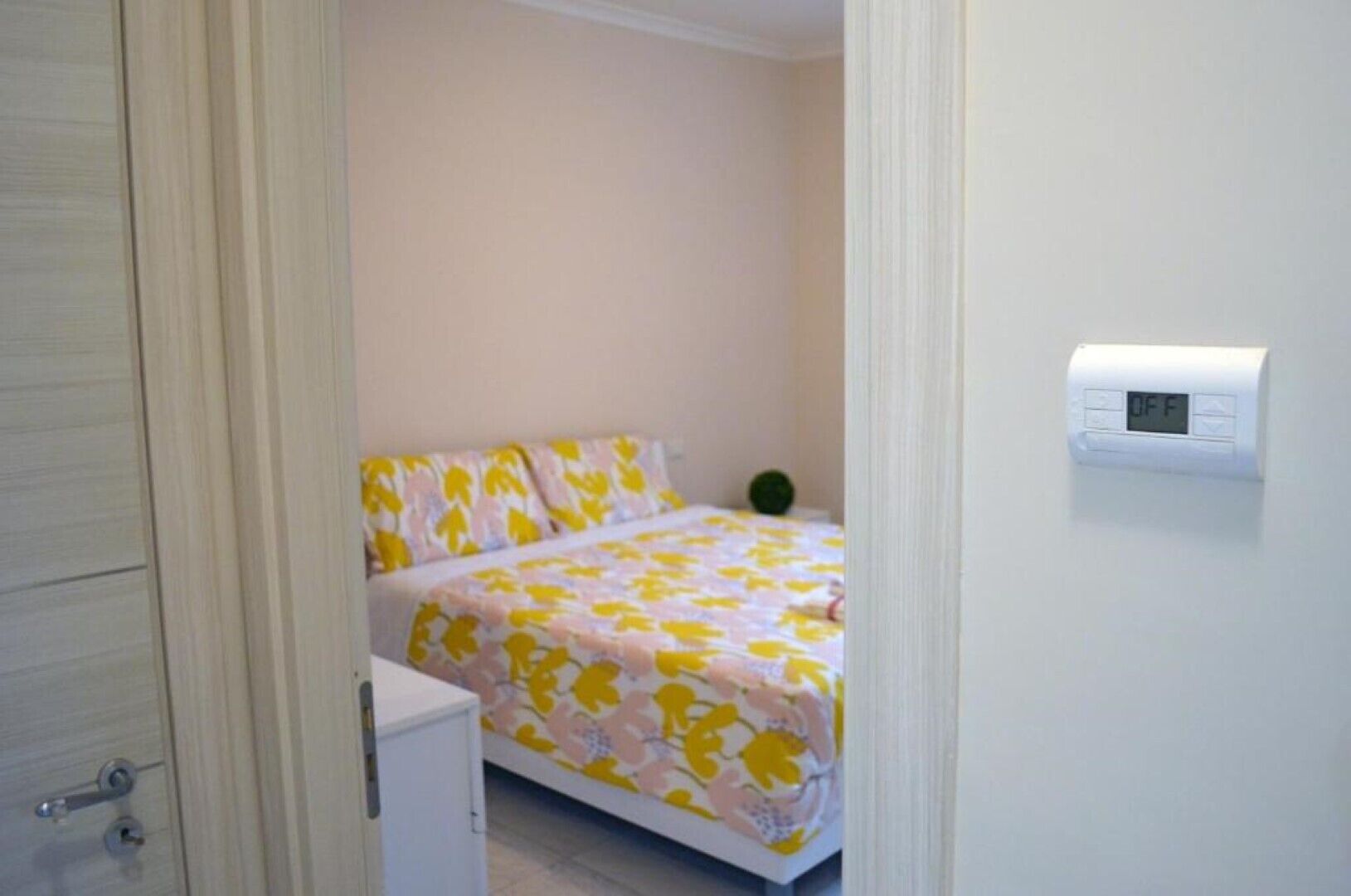 Un dormitorio pequeño con una cama, una mesita de noche y un termostato fijado a la pared.