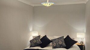 Un dormitorio con cama, dos lámparas de noche, un reloj de pared y una lámpara de techo de vitral.