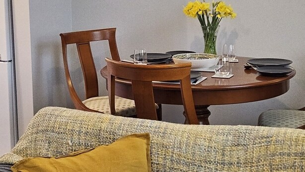 Un comedor con una mesa redonda, sillas y un florero con flores amarillas.