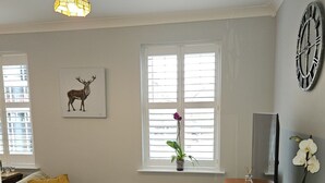 Una sala de estar con sofá, mesa de centro, mueble para televisor, reloj y ventana con persianas.