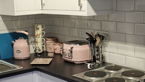Una cocina con una tostadora rosa, una tetera, un portalápices para tazas y un escurreplatos de especias.