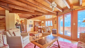 A spacious living room with wooden beams, a fireplace, and large windows offering a mountain view. - Family chalet overlooking the Midi Teeth (Champéry)
