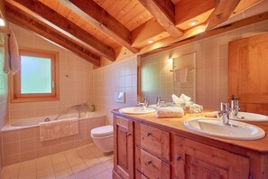 A bathroom with wooden beams, two sinks, a bathtub, and a window.