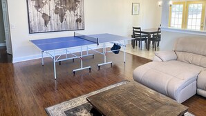 Ett rum med ett bordtennisbord, en stor världskarta som konstverk, en klocka och en beige soffa.