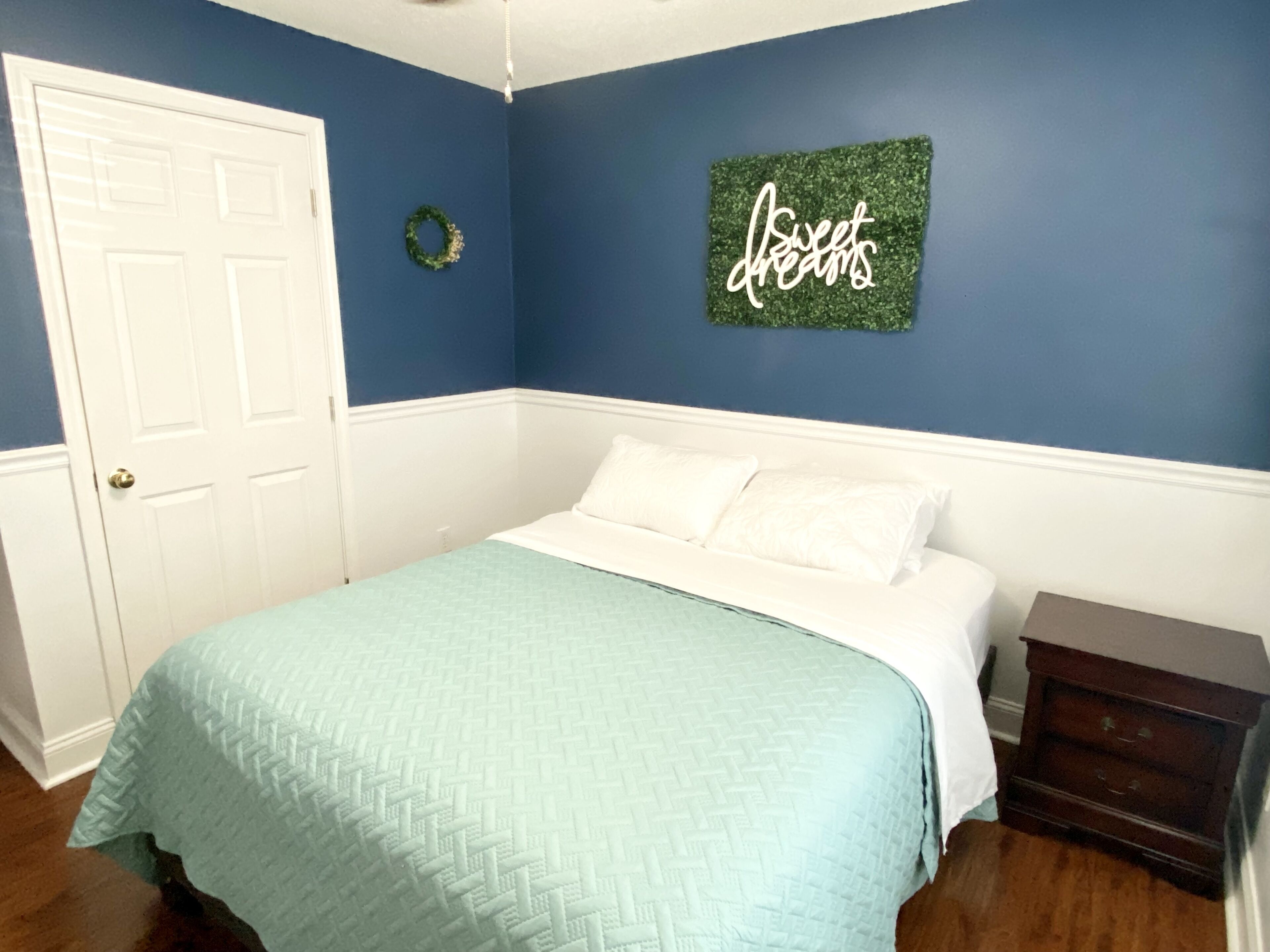 A bedroom with a bed, a dresser, a door, and a wall decoration.