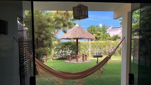 A hammock in a well-maintained garden with a thatched structure and a tiled floor. - LiaMara accommodations, Maragogi - AL (Maragogi)