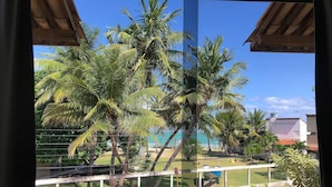 A view from a window overlooking palm trees, a fenced area, and a building with a red roof. - LiaMara accommodations, Maragogi - AL (Maragogi)