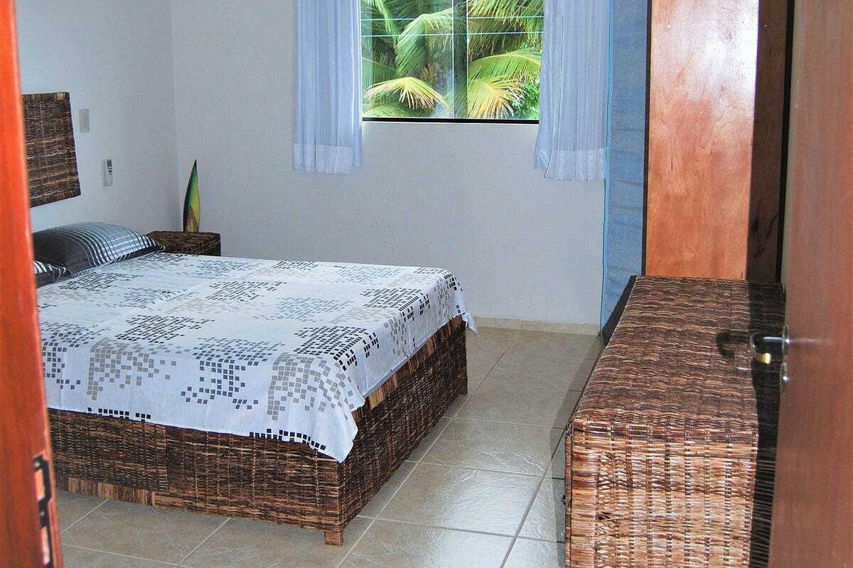 A bedroom with a bed, a nightstand, a dresser, and a window with curtains.