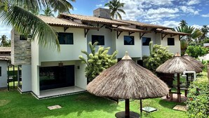 A two-story building with a tiled roof, a covered patio area with thatched umbrellas, and a well-maintained lawn. - LiaMara accommodations, Maragogi - AL (Maragogi)