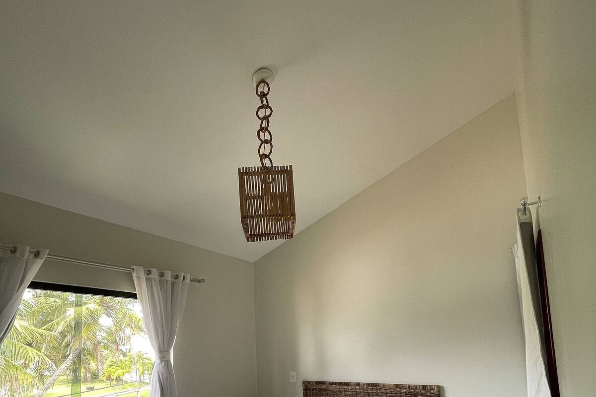 A neatly made bed with white linens, a wicker headboard, and a hanging light fixture.
