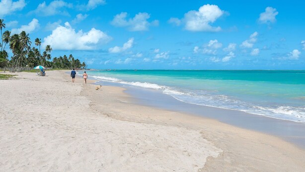 A beach with clear turquoise waters, a sandy shore, and a few people walking. - LiaMara accommodations, Maragogi - AL (Maragogi)