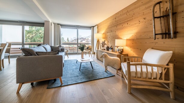 Een moderne woonkamer met een houten wand, een bank, een fauteuil, een bijzettafeltje en een lamp.