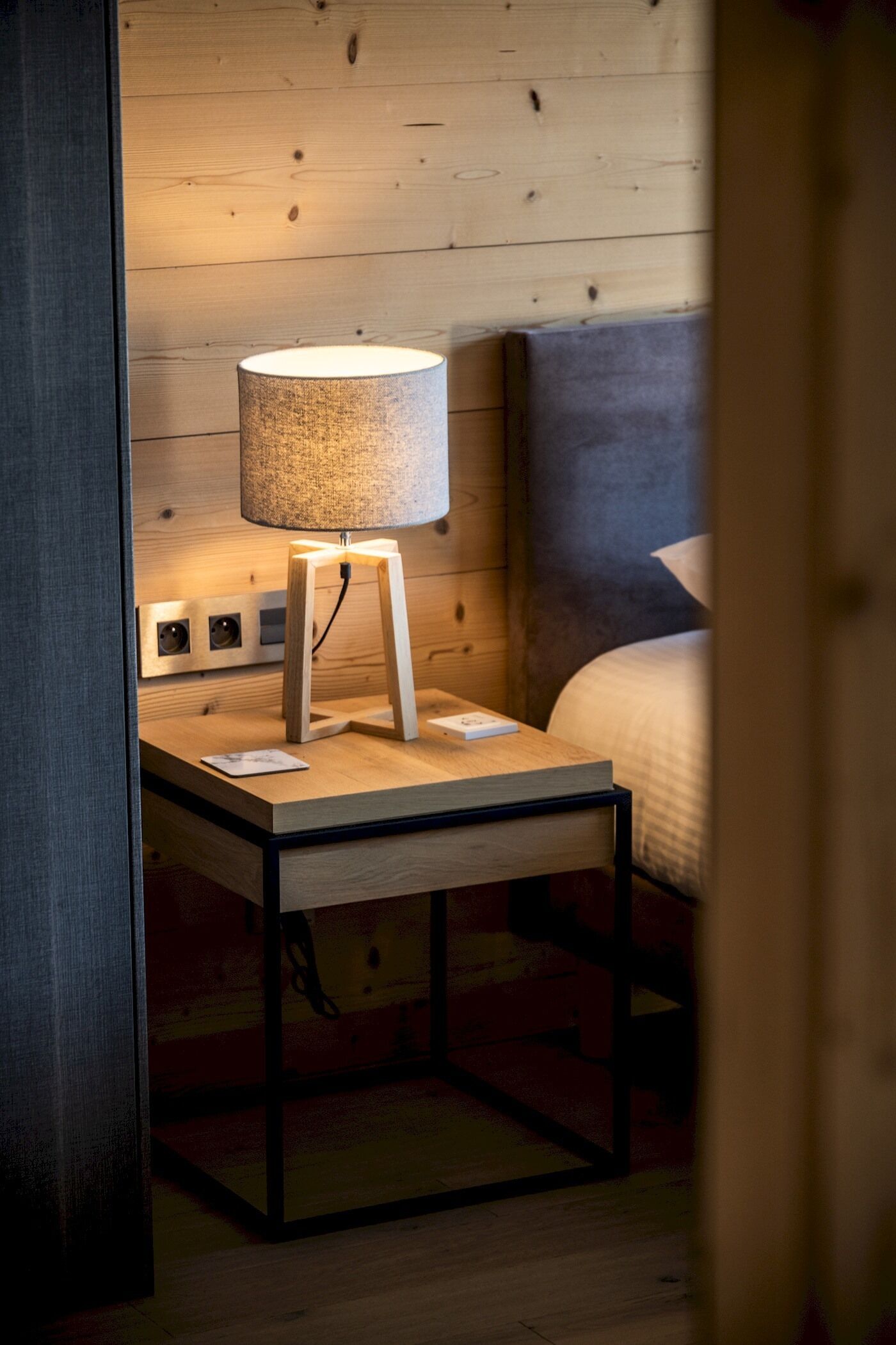 Ein Nachttisch aus Holz mit einer Lampe, einer Steckdose und einer kleinen Karte darauf.