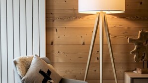 Een moderne kamer met een houten wand, een vloerlamp, een stoel met een zacht kussen en een klein houten kastje.