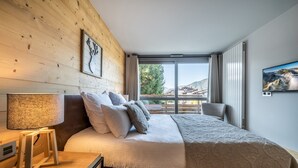 Een slaapkamer met een houten wand, een bed met een gebreide deken, een bedlampje en uitzicht op de omgeving.