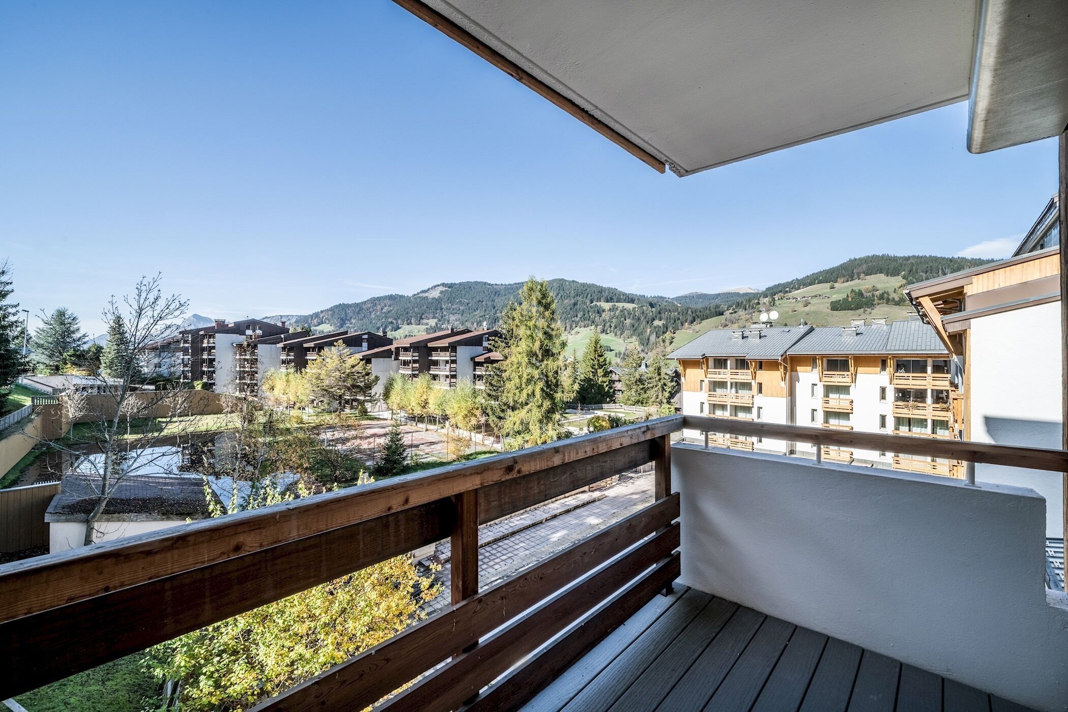 A balcony with a wooden railing overlooking a residential area with buildings and a mountain in the background.