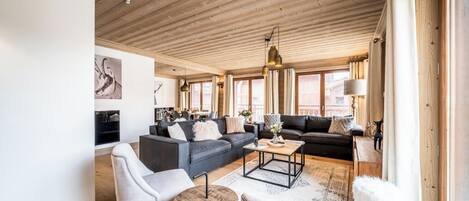 Un salón amplio con techo de madera, un conjunto de sofás, una mesa de centro y una chimenea.