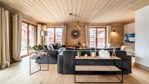 Ein modernes Wohnzimmer mit Holzboden, großen Fenstern, einer Sofagarnitur, einem Couchtisch und einem Fernseher.