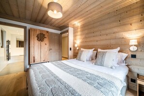 A bedroom with a wooden ceiling, a large bed with a striped blanket, and two bedside lamps.