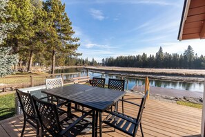A deck with a table and chairs, overlooking a calm lake and dense forest. - ECLI20 - River Front Home on the Deschutes, Pool Table (Sunriver)