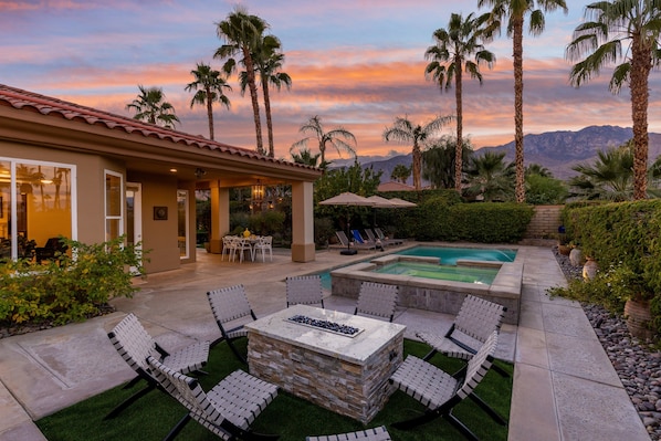 A poolside area with lounge chairs, a fire pit, and a view of mountains.