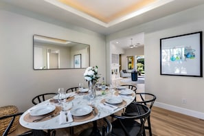 Un coin repas avec une table ronde dressée pour six personnes, un vase rempli de fleurs et une œuvre d’art encadrée accrochée au mur.