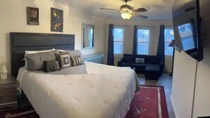 A bedroom with a large bed, a ceiling fan, a dresser, and a window with curtains. - The Most Colorful Home in Atlantic City (Atlantic City)