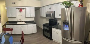 Una cocina moderna con armarios blancos, un refrigerador de acero inoxidable, un microondas y un horno empotrado.