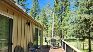 Eine Holzterrasse mit Adirondack-Stühlen und einem Tisch, mit Blick auf eine bewaldete Landschaft.